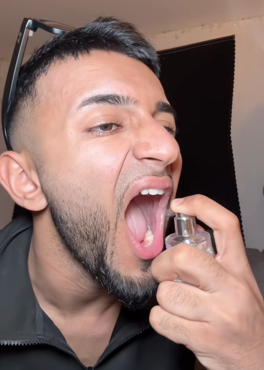 A man spraying freshn into his mouth.